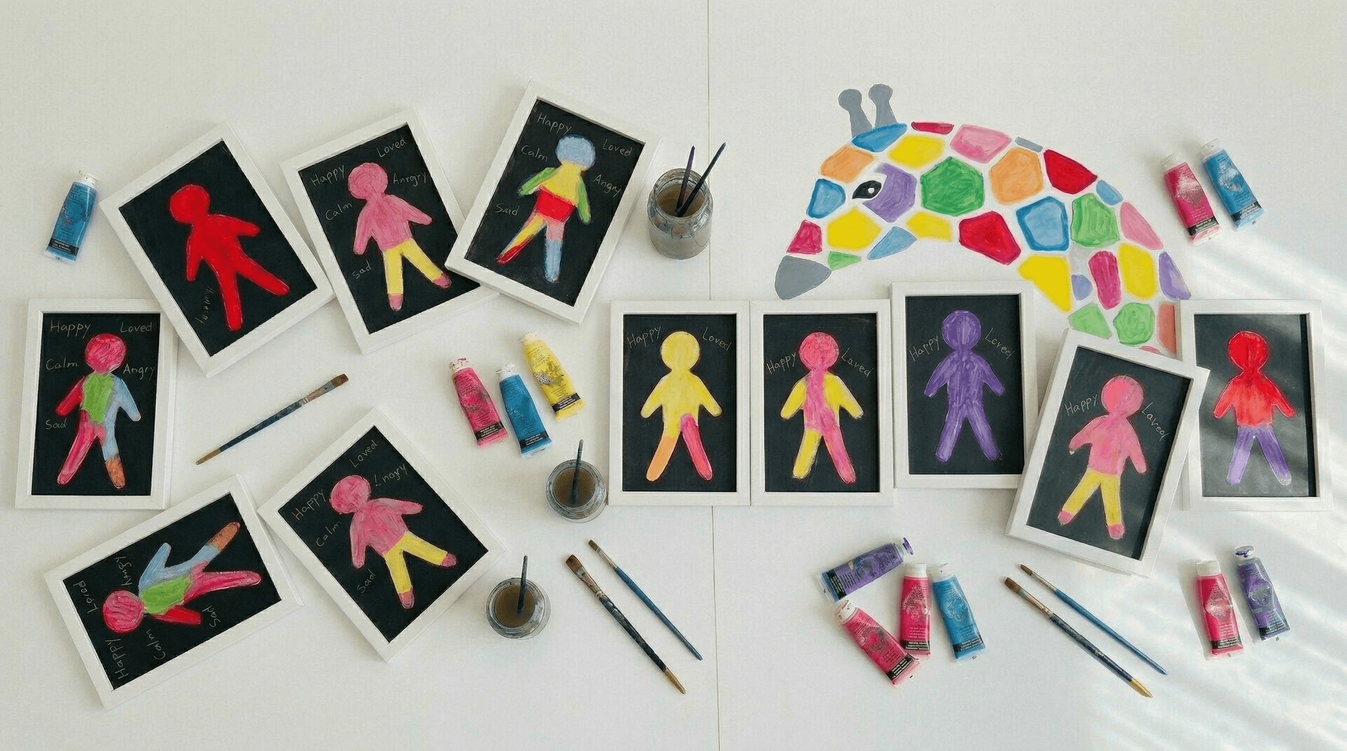 Framed paintings of human figures labeled with emotions, surrounded by paint tubes and brushes.